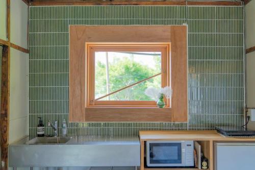 a kitchen with a window above a sink and a microwave at On stay 月見台 in Yokosuka