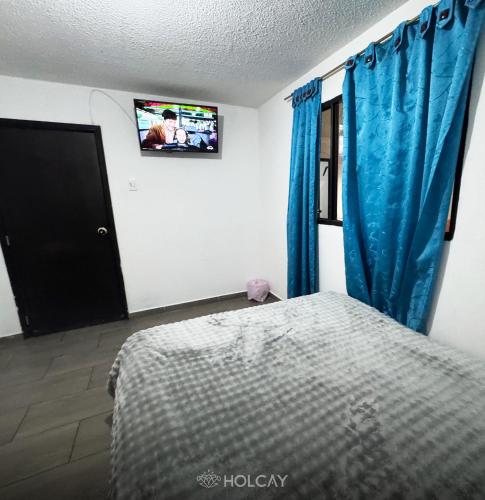 a bedroom with a bed with blue curtains and a tv at Hospedaje Holcay in Bogotá