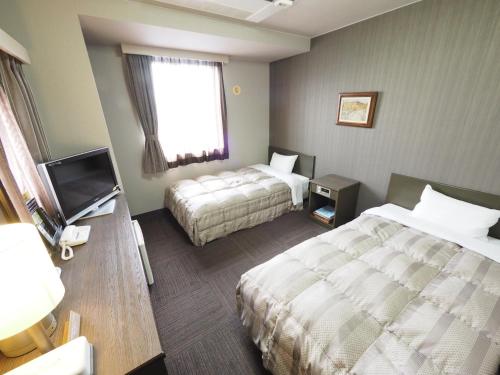 a hotel room with two beds and a television at Hotel Route-Inn Court Matsumoto Inter in Matsumoto