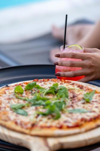 a person holding a drink in front of a pizza at La Luna Hotel in Troulos
