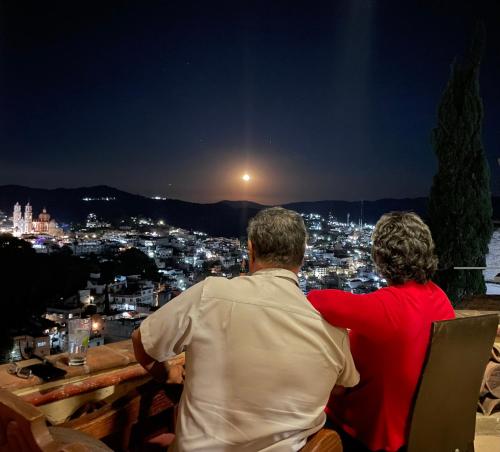 a man and woman sitting on a bench looking at a city at night at Entre el sol y la luna in Taxco de Alarcón