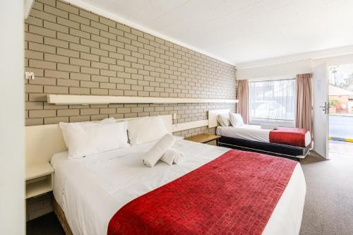 a bedroom with two beds and a brick wall at Wanderlight Motor Inn in Mudgee