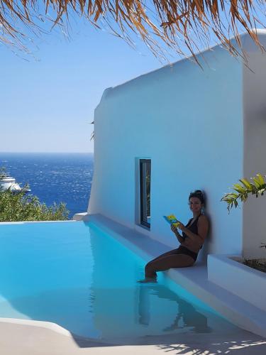 a woman sitting on the edge of a swimming pool at ELLI TROPiCAL LUXURY SUITES SUNSET-INFINITY POOL- SEA SIDE-NEAR CENTER PARKING in Mikonos