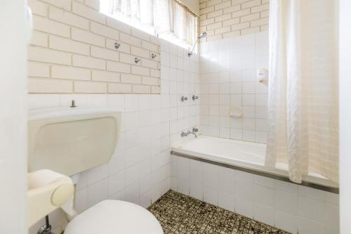 a white bathroom with a toilet and a bath tub at Wanderlight Motor Inn in Mudgee