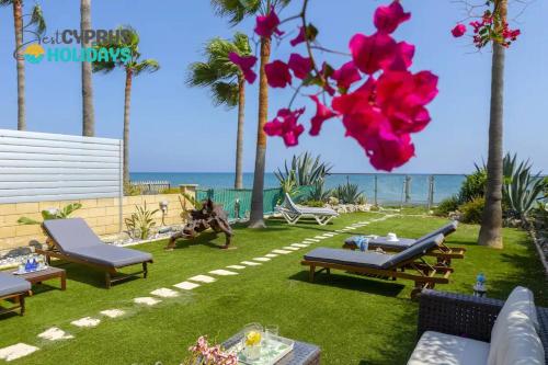 a backyard with chairs and tables and pink flowers at Beachfront Villa Carpe Diem in Kiti