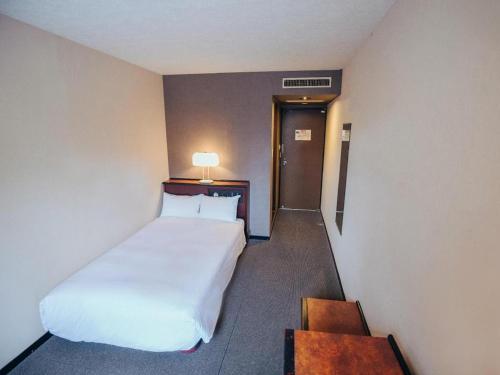 a hotel room with a white bed and a table at Hotel Areaone Miyazaki in Miyazaki