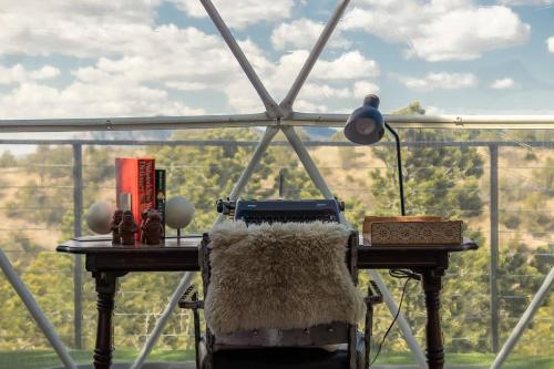 a table with a lamp and a chair in front of a window at Freya Geo Dome Suite At El Mistico Ranch in Nogal