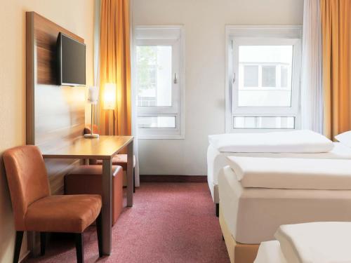 a hotel room with two beds and a desk at B&B HOTEL Mannheim-City in Mannheim