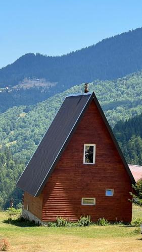 a red barn with a black roof in a field at Villa Horizon - Stunning Mountain Views, Kuqishte in Boge