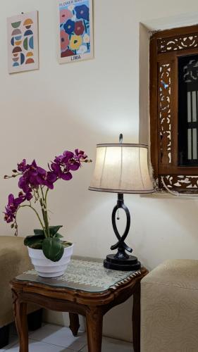 a table with a lamp and a vase of purple flowers on it at Surabaya Homey Dharmahusada Syariah in Surabaya