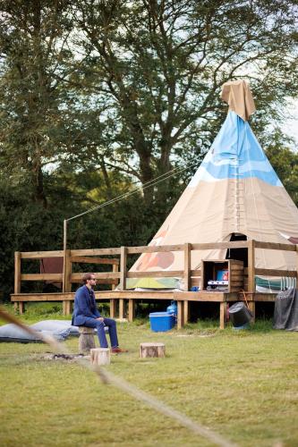 a man sitting on a bench in front of a teepee at Big Sky Tipi Holidays in Wartling