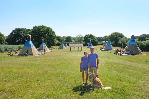 a man and a woman and a dog in a field with tents at Big Sky Tipi Holidays in Wartling