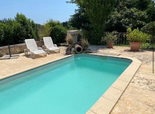 - une piscine avec deux chaises et un chien assis à côté dans l'établissement Villa provençale avec piscine, à Fontvieille