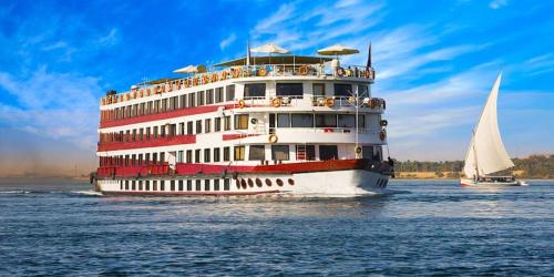 a cruise ship on the water with a sailboat at Bastet Retreat Hotel in Luxor