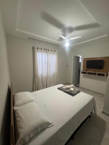 a bedroom with a white bed with a ceiling fan at Pousada 10 de maio in Itaperuna