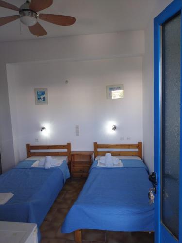 two beds in a room with blue sheets and a fan at Ilios Kalamaki in Kalamaki Heraklion