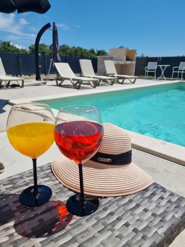 two glasses of wine and a hat next to a swimming pool at Melanie in Mazurija