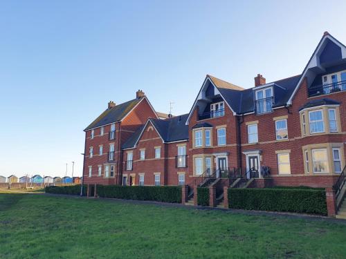 a large red brick building with a green yard at Martello Sunrise - Luxury 3-bedroom Seaview Beach House in Felixstowe