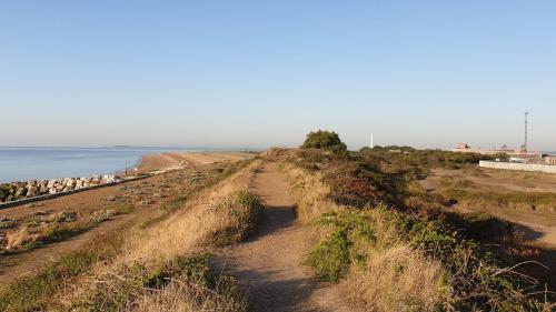 a dirt road leading to a beach next to the ocean at Martello Sunrise - Luxury 3-bedroom Seaview Beach House in Felixstowe