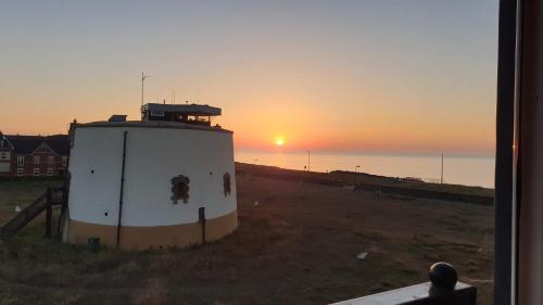 a lighthouse in a field with the sunset in the background at Martello Sunrise - Luxury 3-bedroom Seaview Beach House in Felixstowe
