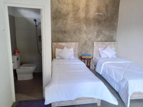two beds in a room with a bathroom with a toilet at Wenten House in Bungbungan