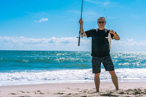 a man standing on the beach holding a fishing pole at 390 Strand Drive in Melbourne Beach