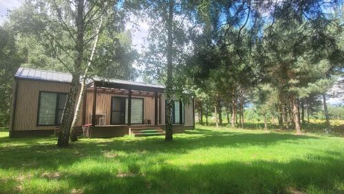 a small cabin in the middle of a field with trees at Wiosłem w Hamaku Domek nad Wkrą 