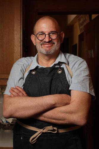 un homme portant des lunettes et un tablier, les bras croisés dans l'établissement Au bon Vivant, à Dampierre-sur-Salon
