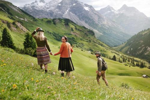 two people walking in a field with mountains in the background at Burg Hotel Oberlech in Lech am Arlberg