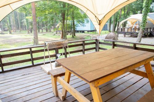 a wooden table and bench on a deck with a tent at 森と湖の楽園ＷorkshopＣampＲesort in Fujikawaguchiko