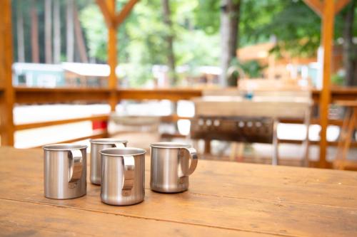 four metal coffee cups sitting on a wooden table at 森と湖の楽園ＷorkshopＣampＲesort in Fujikawaguchiko