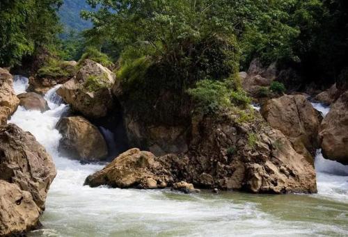 a river with rocks and trees on the side of it at Nam Pé Tày Homestay - View hồ Ba Bể in Bak Kan
