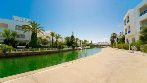 a river with buildings and palm trees next to a street at Lappartement de le Marina 2 : Vue mer et port in Yasmine