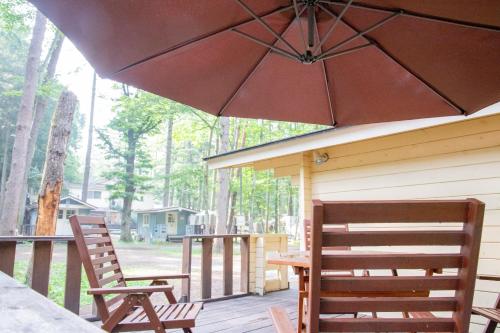 a porch with two chairs and a table and an umbrella at 森と湖の楽園ＷorkshopＣampＲesort in Fujikawaguchiko
