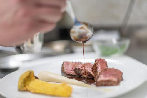 a person drizzling sauce on a piece of meat on a plate at Linara Mountain Family Stay in Valles