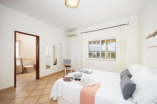 a white bedroom with a bed and a bathroom at Villa Entrecolinas in São Bartolomeu de Messines