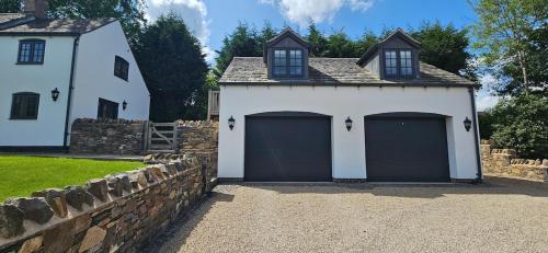 a white house with two garage doors and a stone wall at White Cottage Loft in Newtown Limford