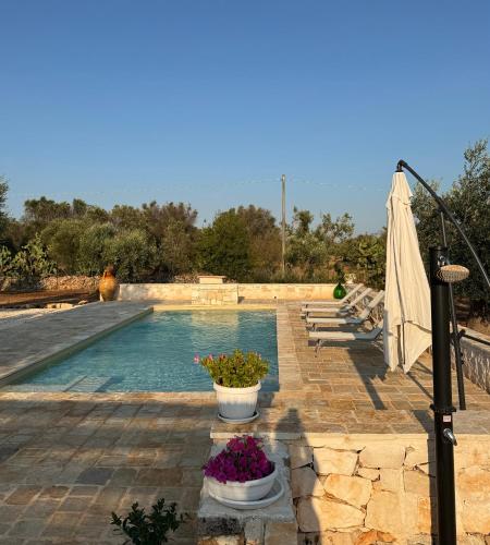 a swimming pool with flowers and an umbrella at Trullo Tatauan in San Michele Salentino