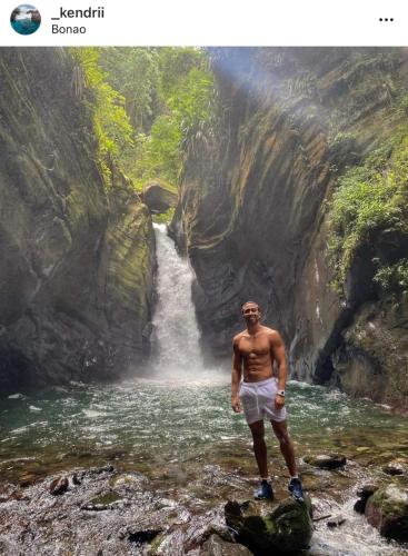 a man standing in a stream in front of a waterfall at Huttub Dailycleaning Gacebo Bbq River in Bonao