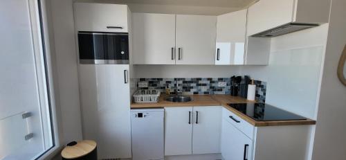 a kitchen with white cabinets and a black microwave at L'écume du fort , Face à la mer, Coucher de soleil in Le Portel