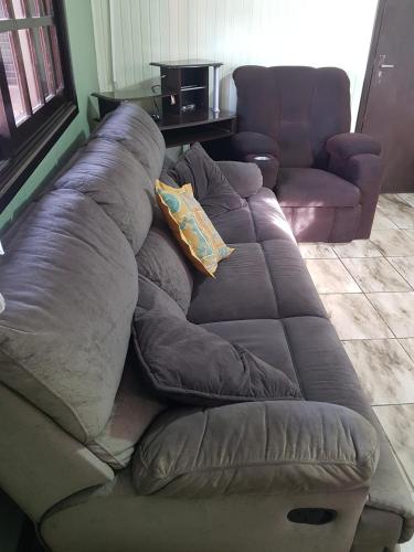 a brown couch with pillows in a living room at CASA COMPLETA CENTRAL, 4 Qtos, Wi-Fi, 130m quadrados, 4 Camas Casal, Churrasqueira Interna, Quintal com Área Verde e Pomar, Varanda, 2 Banheiros, 9 Pessoas, Área Frontal, Garagem Coberta, Estacion Interno 2 Carros, Fogão a Lenha in Cambará