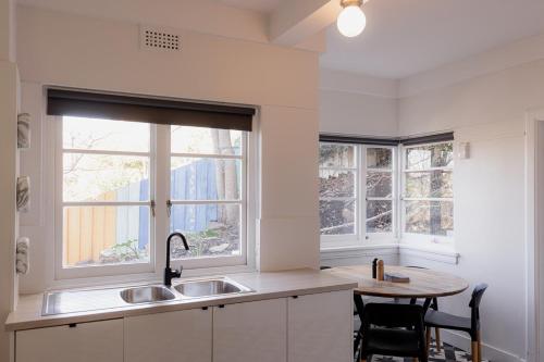a kitchen with a sink and a table and two windows at Light and Bright Trevallyn Stay with River Views in Royal Park