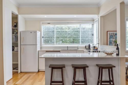 a kitchen with a white refrigerator and two bar stools at Bowen View - pet-friendly home near Hyams Beach in Hyams Beach