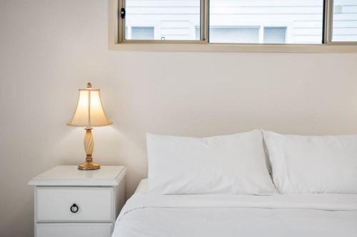 a white bed with a lamp on a night stand at Footprints at Hyams Beach - 4BR home w. games room in Hyams Beach