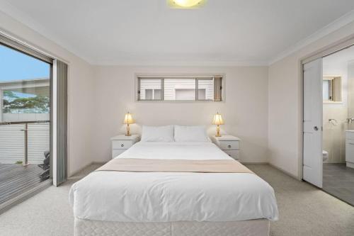 a white bedroom with a large bed and a balcony at Footprints at Hyams Beach - 4BR home w. games room in Hyams Beach