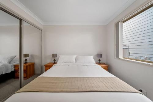 a white bedroom with a large bed and a window at Footprints at Hyams Beach - 4BR home w. games room in Hyams Beach