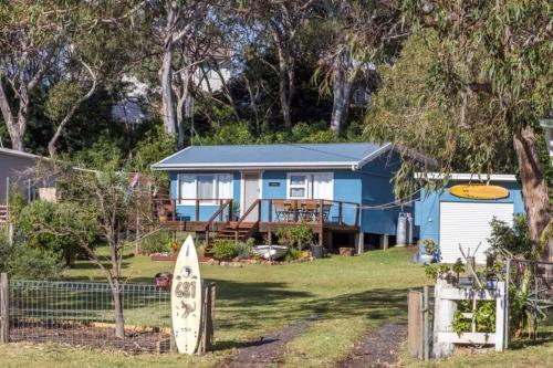 une maison bleue avec une planche de surf devant elle dans l'établissement Retro Beach Cottage - classic surf getaway, à Kioloa