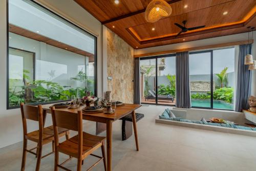 a dining room with a table and chairs and large windows at Greha Natha Villa Ubud in Ubud
