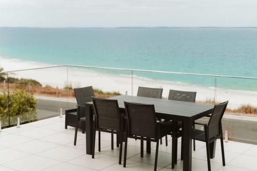 a black dining table and chairs with a view of the ocean at Allure at Hyams Beach - seconds to white sands in Hyams Beach