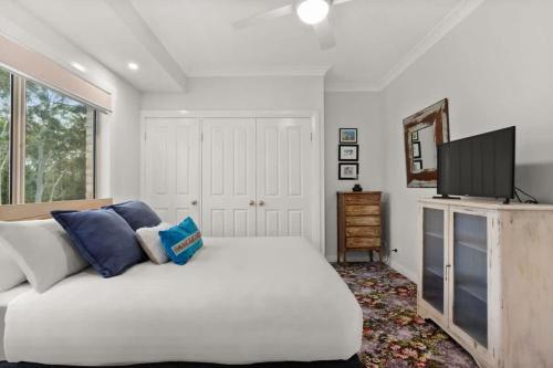 a bedroom with a white bed and a flat screen tv at Sanctuary Lodge - 5BR waterfront country getaway in Sanctuary Point